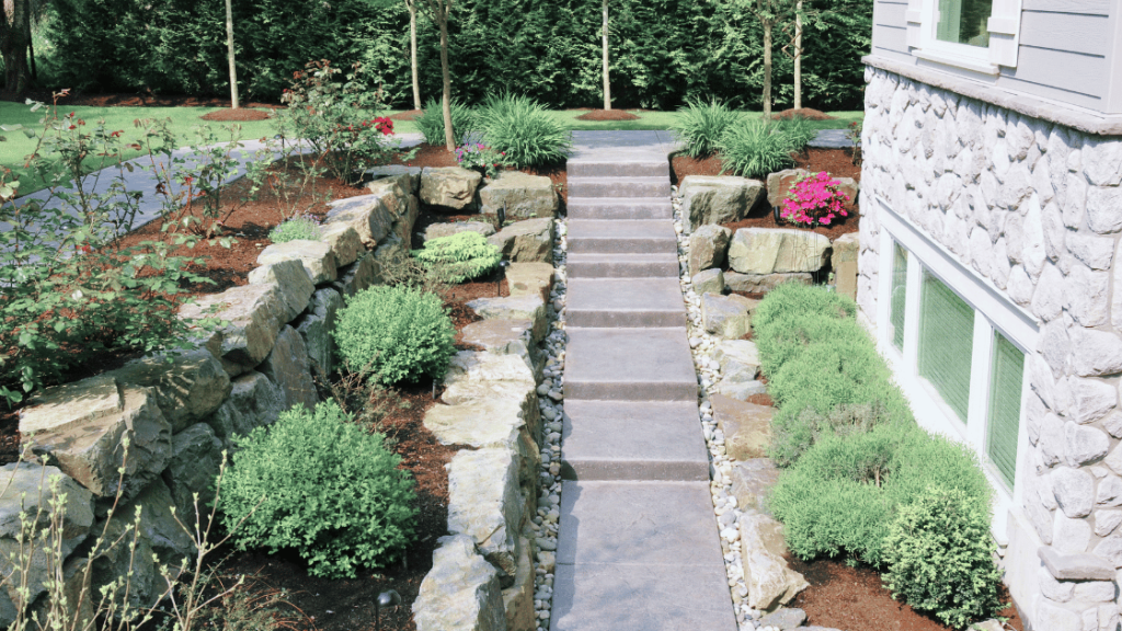 A concrete pathway with landscaping by a house